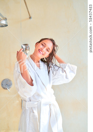 Photo of happy brunette woman with wet hair in white bathrobe standing in bath. 58437483