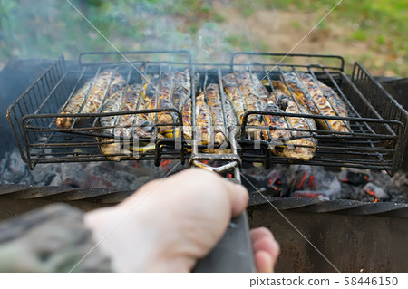 hand of a man holding a grill with fried fish hand of a man holding a grill with fried fish 58446150