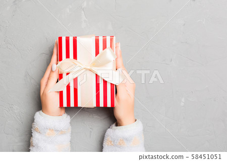 Woman arms holding gift box with colored ribbon on 58451051