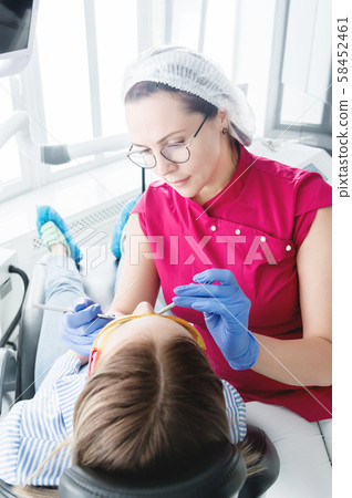 In the dentist's office. A female dentist in glasses is preparing to make a cast of the jaw of a In the dentist's office. A female dentist in glasses is preparing to make a cast of the jaw of a 58452461