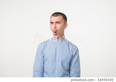 Shocked face of caucasian young man in blue shirt on grey background Shocked face of caucasian young man in blue shirt on grey background 58456509