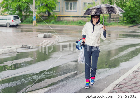 Young adult woman wearing casual sport clothes crossing road holding umbrella in hand during rain in Young adult woman wearing casual sport clothes crossing road holding umbrella in hand during rain in 58458032
