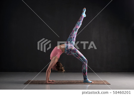Woman practices yoga asana eka pada chakrasana or one legged wheel pose Woman practices yoga asana eka pada chakrasana or one legged wheel pose 58460201
