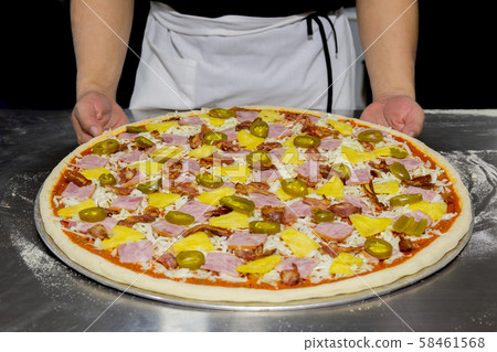 Chefs hand with hawaiian pizza and pineapple, pickled chilli ,ham on the table. 58461568