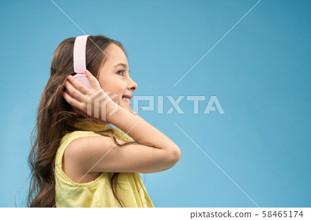Little girl wearing earphones, listening music and smiling Little girl wearing earphones, listening music and smiling 58465174