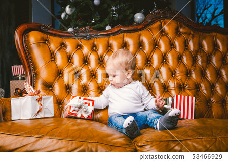 Happy little smiling boy with christmas gift box. Beautiful little baby, sits on asofa with gift 58466929