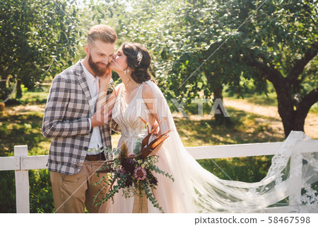 Caucasian couple in love bride and groom standing in embrace near wooden white, rural fence in park 58467598