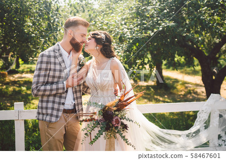 Caucasian couple in love bride and groom standing in embrace near wooden white, rural fence in park Caucasian couple in love bride and groom standing in embrace near wooden white, rural fence in park 58467601