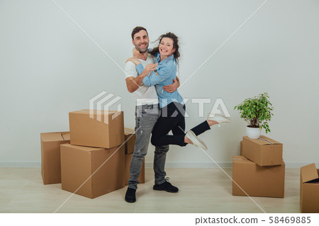 Couple moving into their new house. Woman is very glad and is hanging on her husband's neck, hugging 58469885