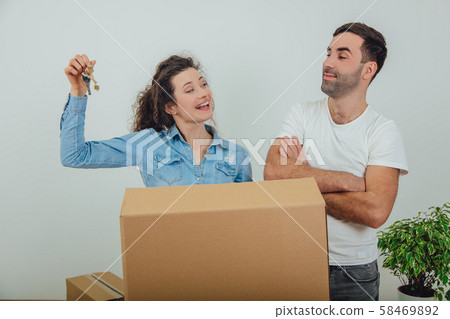 Young wife and husband standing behind the big carton box, together. Woman is holding keys to their Young wife and husband standing behind the big carton box, together. Woman is holding keys to their 58469892
