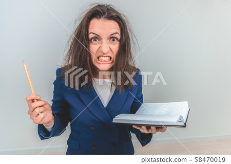 Insane young teacher with tousled hair, holding notebook and pen, setting her teeth, looking out of 58470019