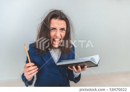 Exhausted young teacher with tousled hair holdingnotebook and pen, leaning to the camera, screaming Exhausted young teacher with tousled hair holdingnotebook and pen, leaning to the camera, screaming 58470022