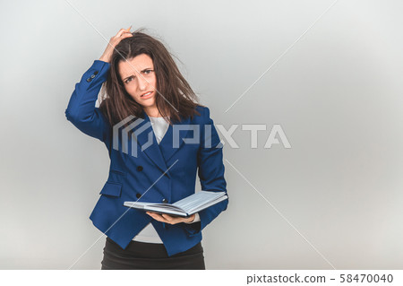 Upset female teacher standing with notebook in hands, keeping hand on the head, looking tired 58470040