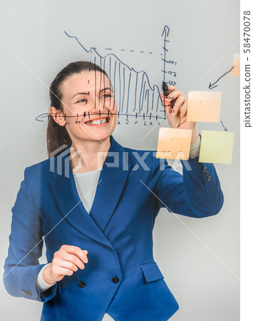 Inspired woman in formal suit, drawing diagram on the glass, smiling. Inspired woman in formal suit, drawing diagram on the glass, smiling. 58470078