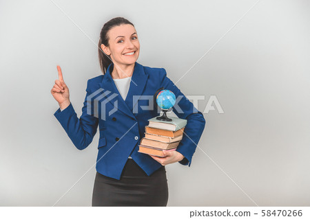 Happy female teacher holding a stack of colorful books, pointing her finger up, calling to pay Happy female teacher holding a stack of colorful books, pointing her finger up, calling to pay 58470266