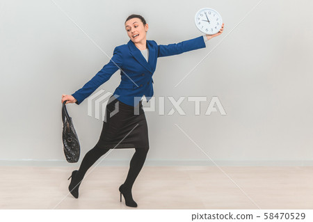 Young teacher in formal suit with bag, holding a white clock, running because she is late. 58470529