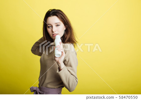 Image of a happy young girl standing isolated on a yellow background singing in a yogurt bottle 58470550