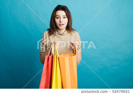 Image of happy young girl standing on blue background with shopping bags Image of happy young girl standing on blue background with shopping bags 58470681