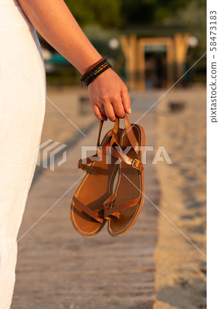 Woman holds brown leather sandals in her hand and Woman holds brown leather sandals in her hand and 58473183