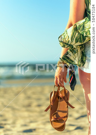 Woman holds brown leather sandals in her hand and 58473184