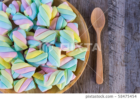 Multi-colored Marshmallow twist in a wooden dish with spoon on a wooden background. Copy space background and texture Multi-colored Marshmallow twist in a wooden dish with spoon on a wooden background. Copy space background and texture 58475454