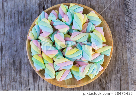 Multi-colored Marshmallow twist in a wooden dish on a wooden background. Copy space background and texture Multi-colored Marshmallow twist in a wooden dish on a wooden background. Copy space background and texture 58475455