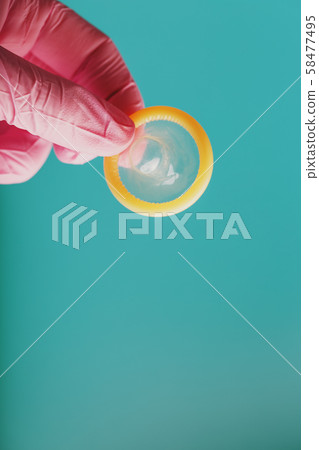 An opened condom in a hand in a pink glove holds An opened condom in a hand in a pink glove holds 58477495