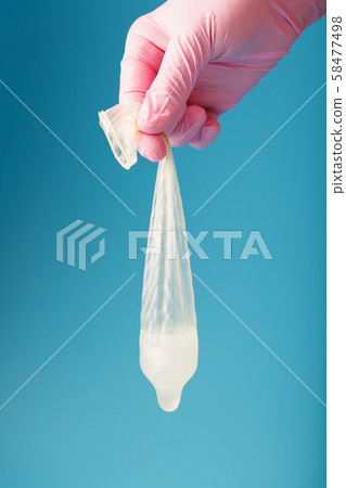 Used condom with sprema in hand, in a pink glove 58477498