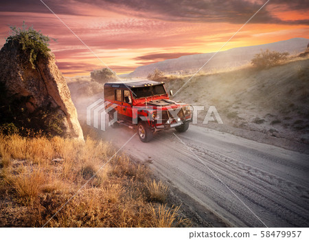 Red off-road car on dusty road near the cliff 58479957