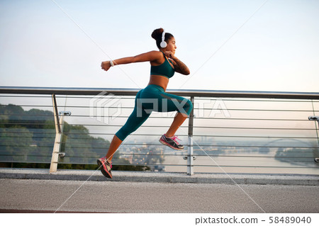 Dark-skinned woman wearing white earphones running fast Dark-skinned woman wearing white earphones running fast 58489040