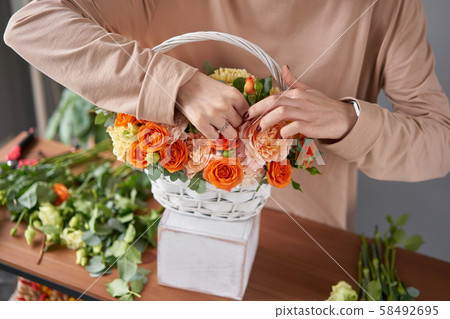 Florist woman creates flower arrangement in a wicker basket. Beautiful bouquet of mixed flowers Florist woman creates flower arrangement in a wicker basket. Beautiful bouquet of mixed flowers 58492695
