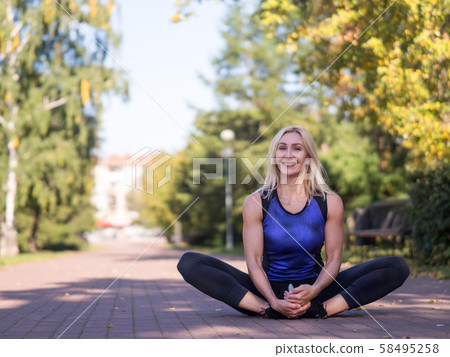 Smiling woman sitting on the pavement and stretching outdoor in urban park, selective focus 58495258