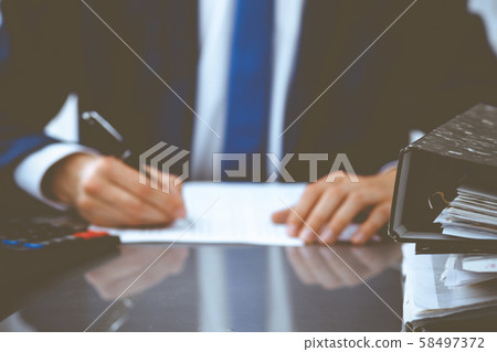 Binders with papers waiting to be processed with businessman or bookkeeper back in blur. Accounting 58497372