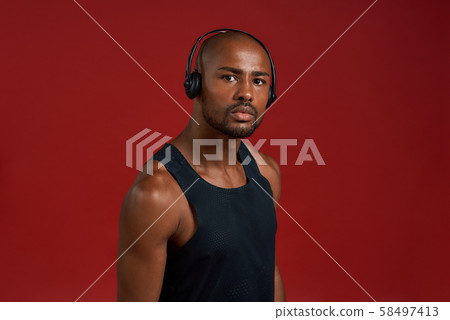 Portrait of handsome sporty afro american man in headphones looking at camera while standing against 58497413