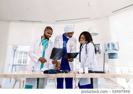 Healthcare, medical: Group of three young African doctors, two men and woman, discuss and looking x 58497949