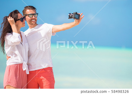 Happy couple taking a photo on white beach on honeymoon holiday Happy couple taking a photo on white beach on honeymoon holiday 58498326