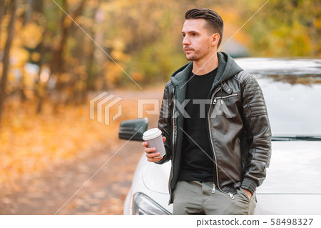Young man drinking coffee with phone in autumn park outdoors Young man drinking coffee with phone in autumn park outdoors 58498327