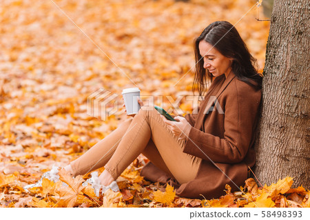 Fall concept - beautiful woman drinking coffee in autumn park under fall foliage Fall concept - beautiful woman drinking coffee in autumn park under fall foliage 58498393