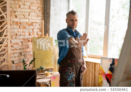 Creative painter in workwear covering part of painting with hand 58500461