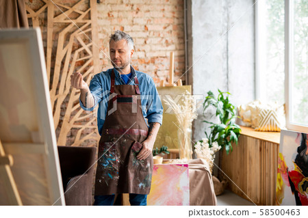 Professional painter in workwear determining center of painting on easel 58500463