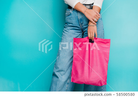 Lower part of young casual female shopper in blue jeans holding fucsia pink bag Lower part of young casual female shopper in blue jeans holding fucsia pink bag 58500580
