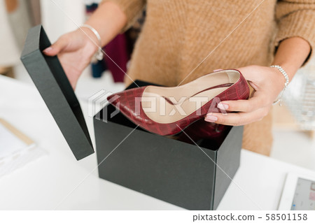 Young female customer unpacking black box and taking out stylish leather shoes Young female customer unpacking black box and taking out stylish leather shoes 58501158