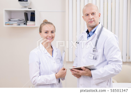Happy young successful clinician and her bald serious colleague in whitecoats 58501347