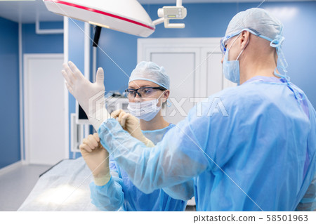 Young assistant in uniform helping surgeon put on medical gloves 58501963