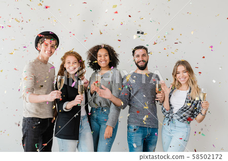 Young ecstatic multiracial friends cheering up with champagne in confetti Young ecstatic multiracial friends cheering up with champagne in confetti 58502172
