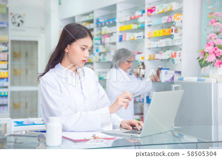 Attractive young female pharmacist checking stock at the drugstore on computer notebook Attractive young female pharmacist checking stock at the drugstore on computer notebook 58505304