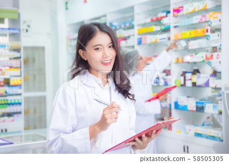 Beautiful asian pharmacist holding chart and smiles in drugstore Beautiful asian pharmacist holding chart and smiles in drugstore 58505305