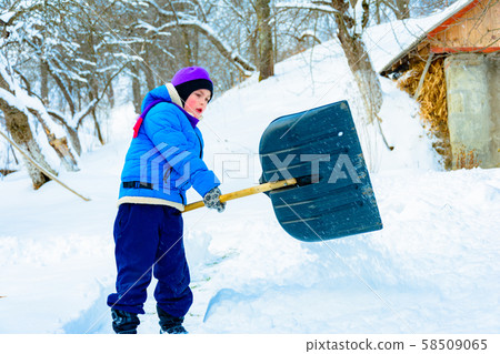After heavy snow, the little boy clears the snow with a shovel. 58509065