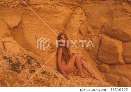 Young woman sitting on sand stone in beige body Young woman sitting on sand stone in beige body 58510595