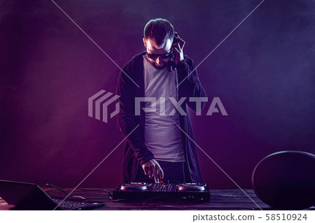 Trendy male dj posing against mixing console Trendy male dj posing against mixing console 58510924